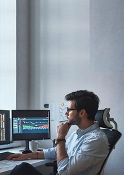 An image of a professional analysing multiple computer screens displaying market and risk data representing energy and commodity risk analytics