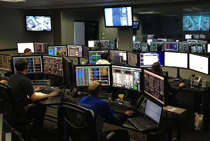 A high-tech room filled with multiple computers and large screens displaying market and risk data representing energy and commodity risk analytics.